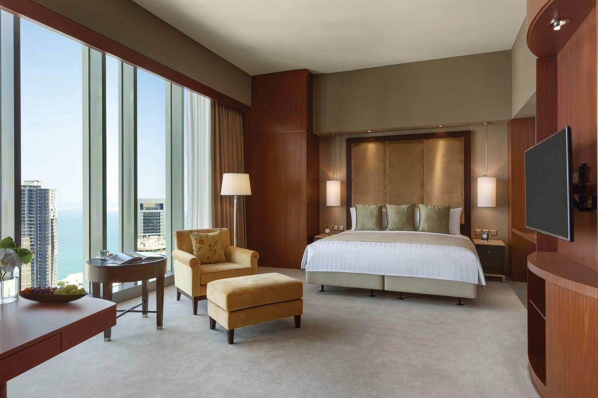 A hotel room with a large bed, a desk with a chair, a small table, and a TV.