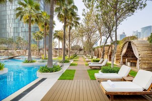 Área de piscina com espreguiçadeiras, deck de madeira e vista para edifícios modernos.