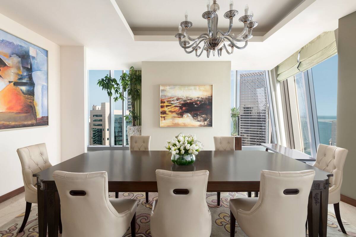 A dining room with a large table, six chairs, a chandelier, and artwork on the walls.