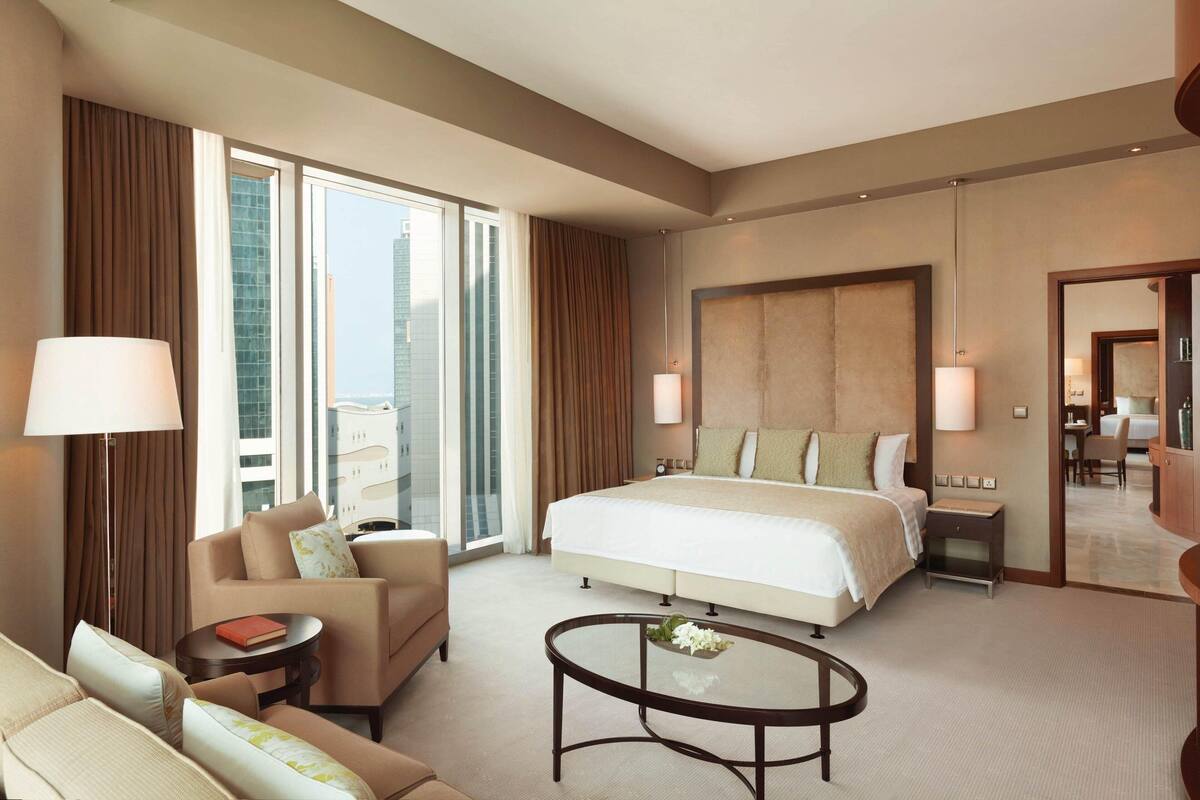 A hotel room with a large bed, a sofa, a coffee table, and a view of the city.