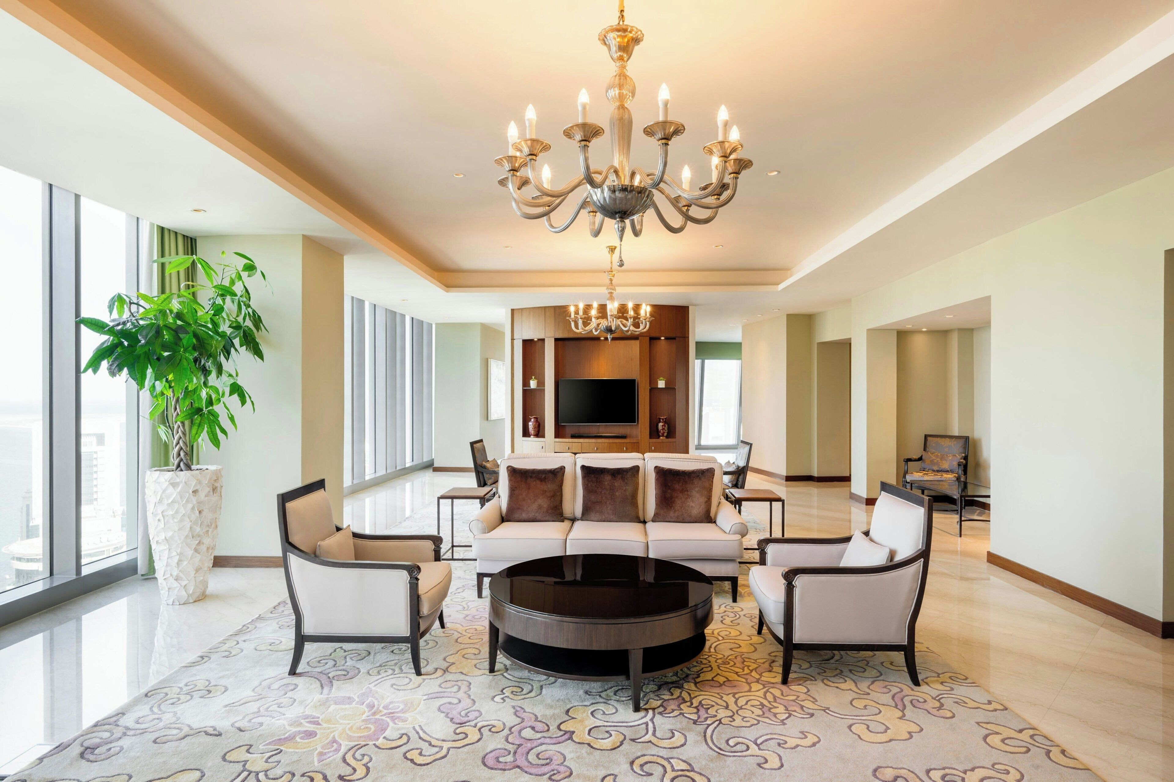 A spacious living room with a large chandelier, a sofa set, a coffee table, and a large potted plant.