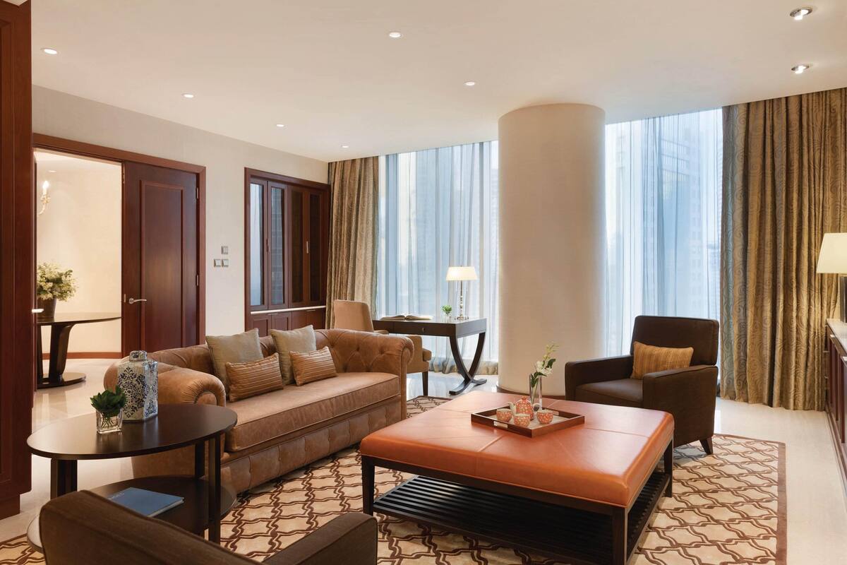 A modern hotel room with a sofa, armchair, coffee table, and a large window with curtains.