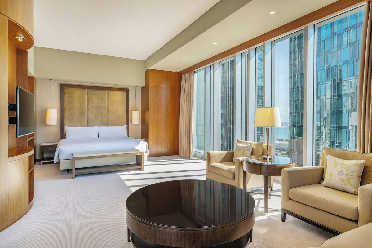 A modern hotel room with a large bed, a round coffee table, a sofa, and a TV.