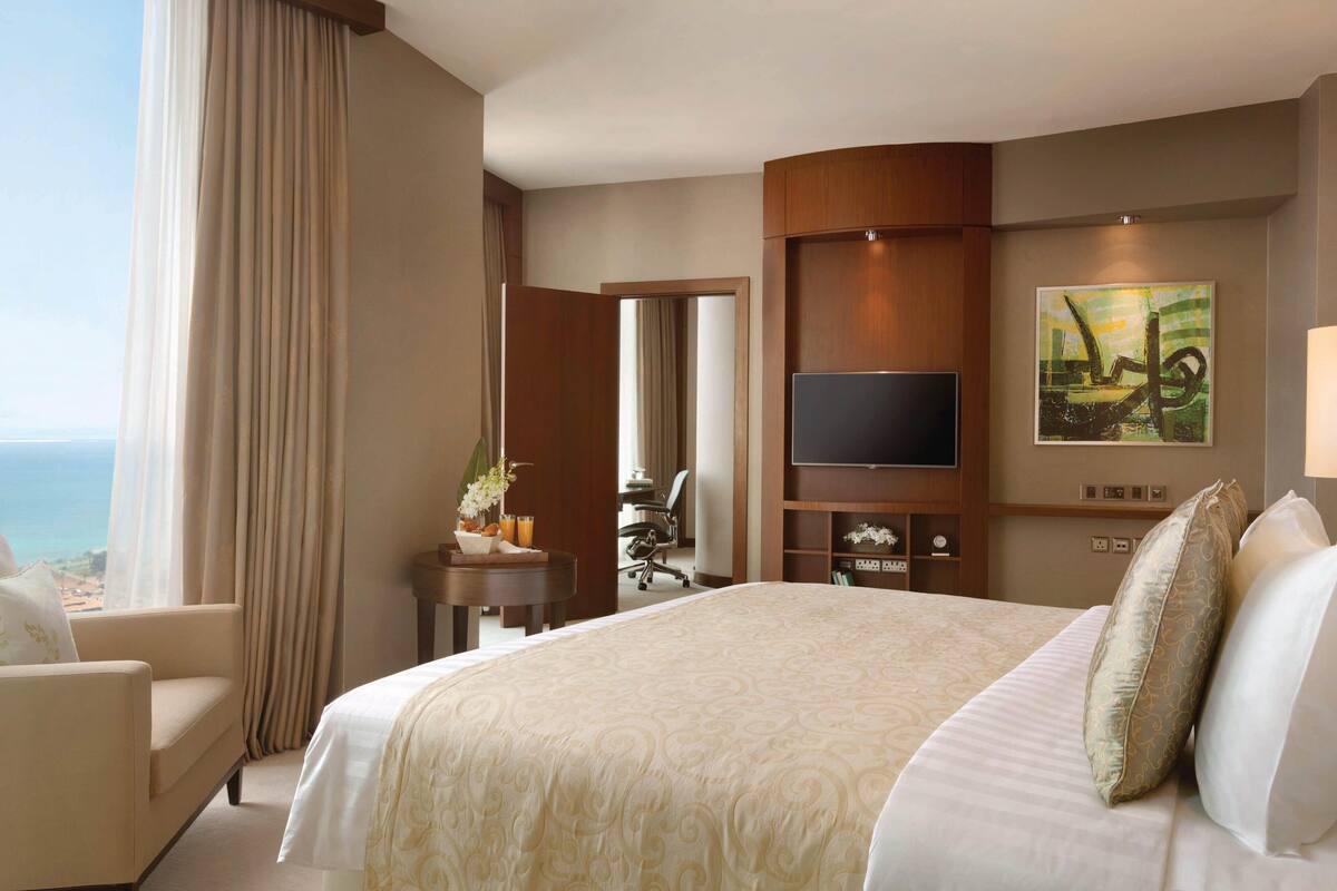A hotel room with a large bed, a TV, a desk with a chair, and a view of the ocean.