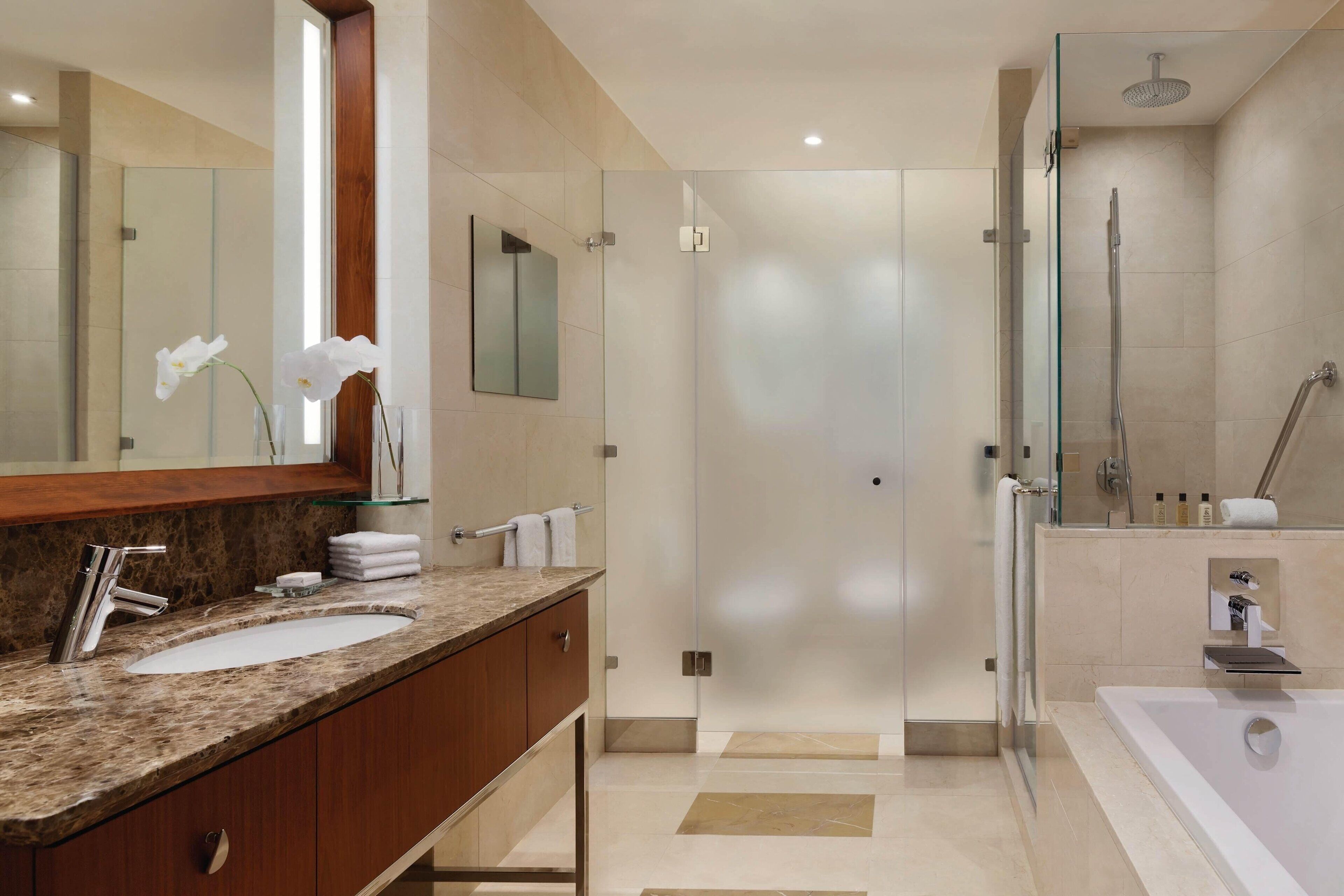 Un bagno moderno con lavabo in marmo, cabina doccia in vetro e un grande specchio.