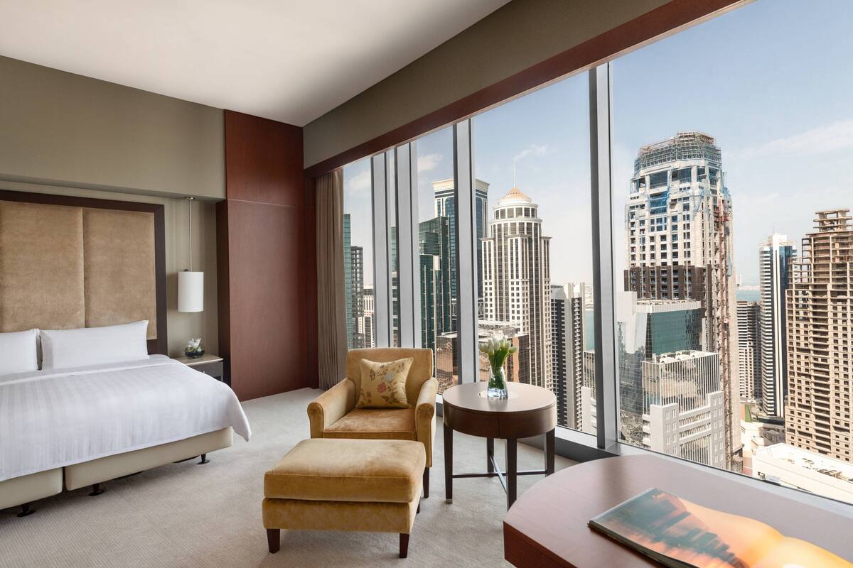 A hotel room with a large bed, a sofa, a small table, and a view of the cityscape.