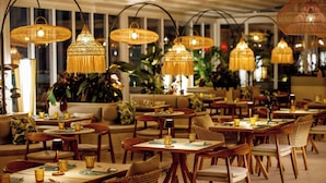 Un restaurante con varias mesas y sillas, iluminación cálida y lámparas colgantes.