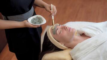 A person receiving a facial treatment with a brush, in a room with wooden flooring.