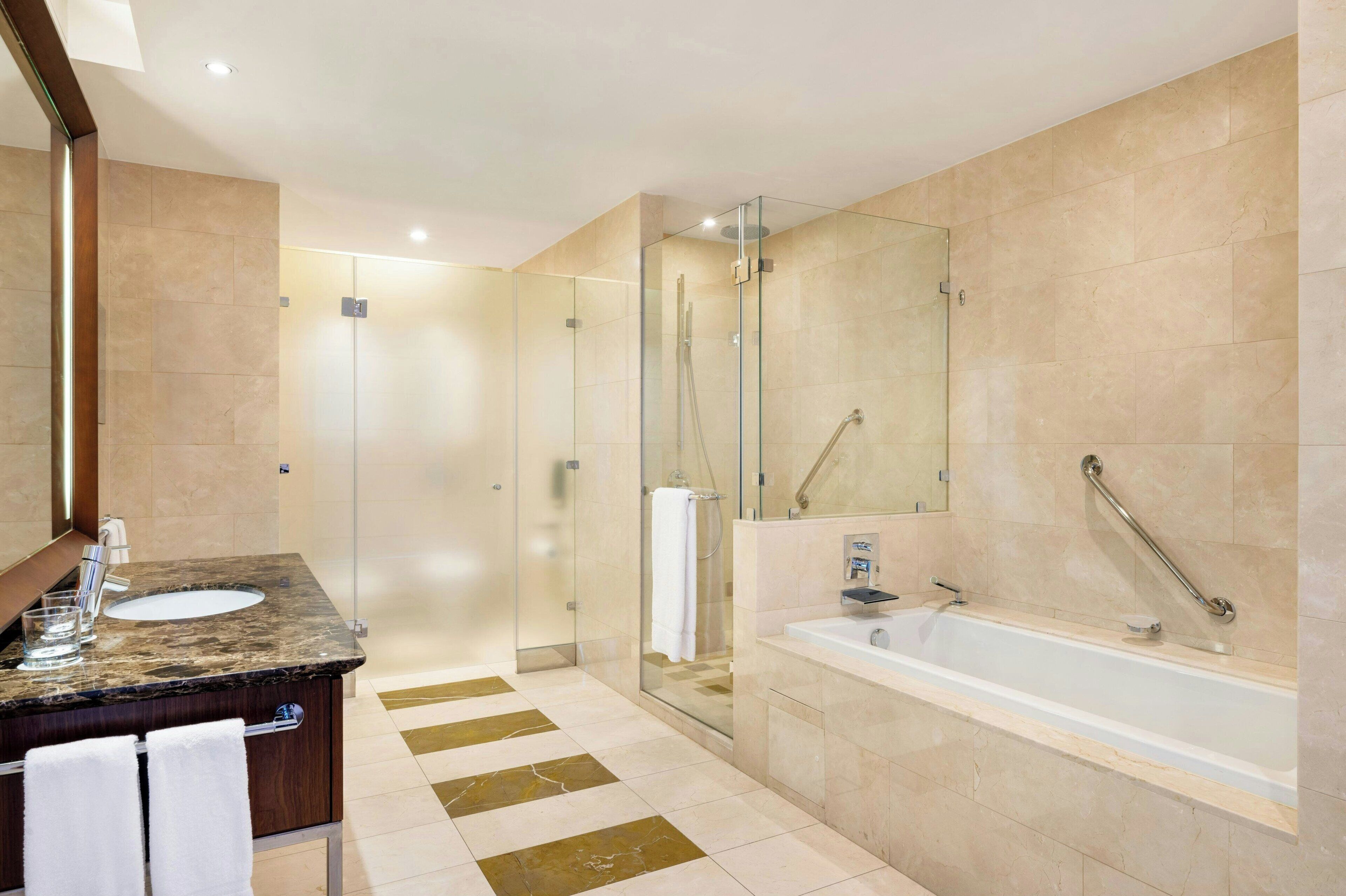 A modern bathroom with a glass-enclosed shower, a marble sink, and a large bathtub.