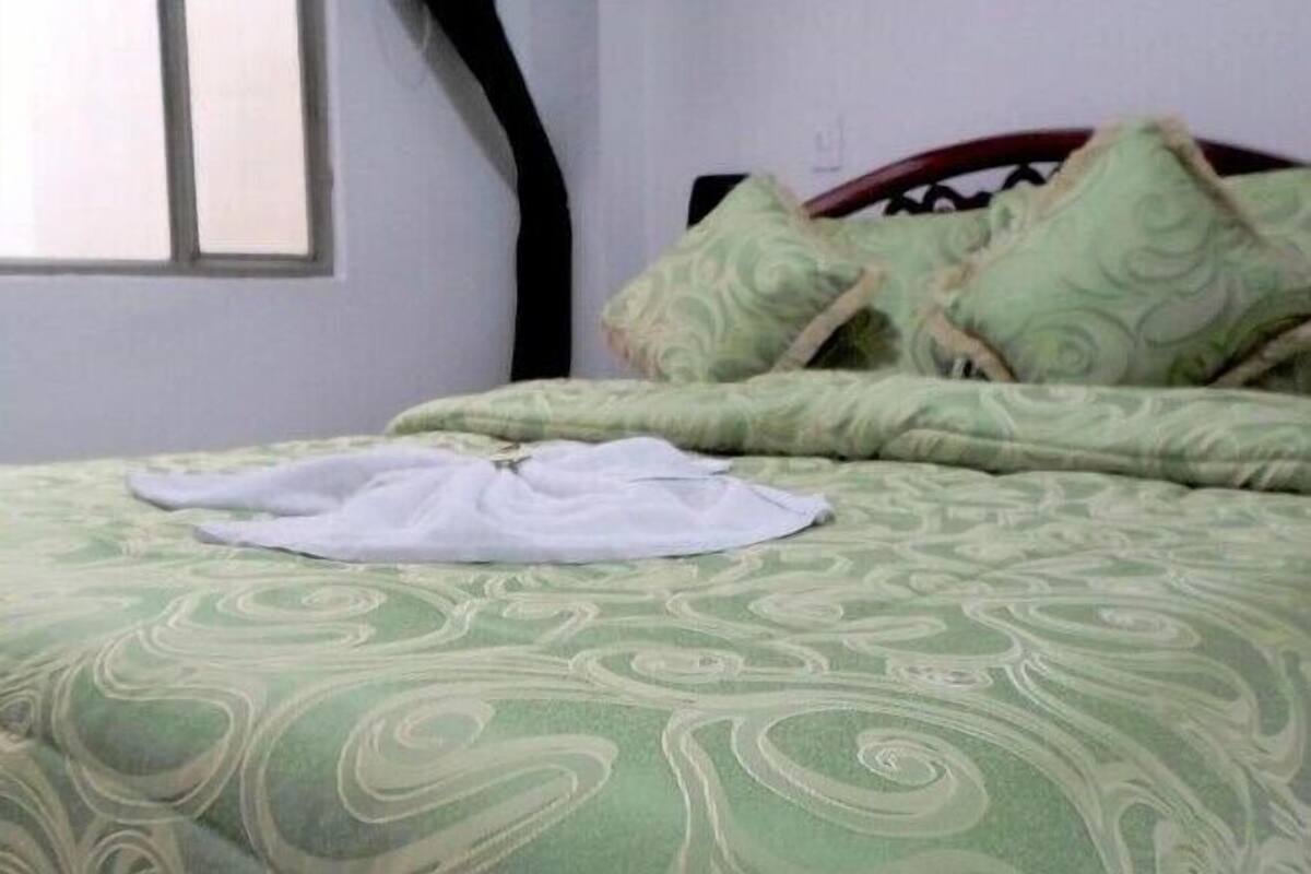 A neatly made bed with a green patterned bedspread and pillows, a white blanket, and a wooden headboard.