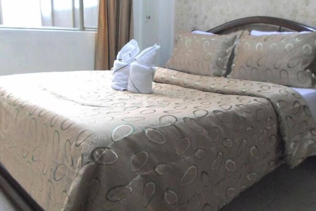 A hotel room with a bed covered in patterned bedding, a neatly made bed with a towel, and a window with curtains.