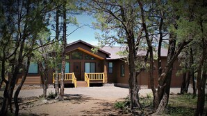 A cabin with a wooden exterior, a porch with yellow railings, and a gravel driveway surrounded by trees. - Custom built cabin sitting on several acres lot in Pinetop-Lakeside! (Pinetop-Lakeside)