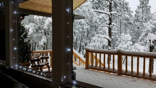 A wooden deck with a railing, a Christmas tree, and snow-covered trees in the background. - Custom built cabin sitting on several acres lot in Pinetop-Lakeside! (Pinetop-Lakeside)
