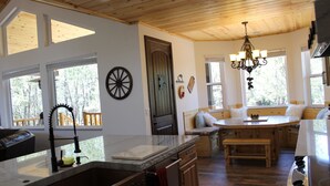 A kitchen with a wooden ceiling, a large window, a chandelier, and a dining area with a bench. - Custom built cabin sitting on several acres lot in Pinetop-Lakeside! (Pinetop-Lakeside)