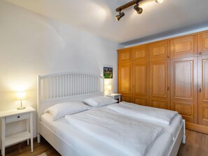 A bedroom with a white bed, wooden wardrobe, and bedside lamps.