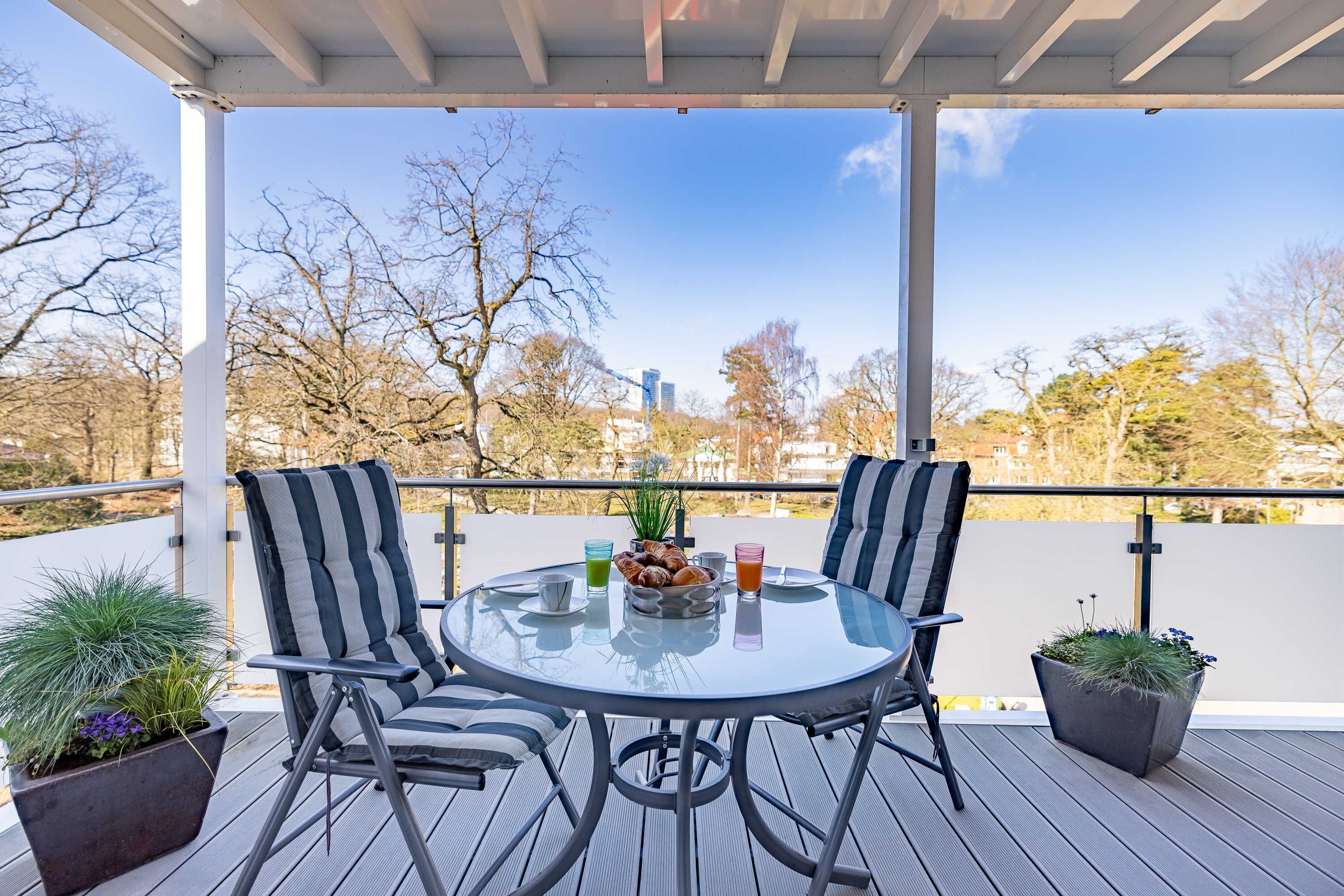 A covered outdoor seating area with a round table, two chairs, and potted plants.