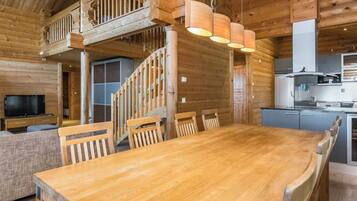 A wooden interior with a dining table, chairs, a TV, and a kitchen area.