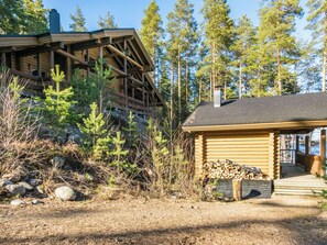 Une cabane dotée d’une terrasse en bois et d’un porche couvert, entourée d’arbres et bordée d’un sol rocheux.