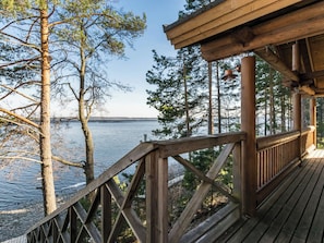Une terrasse en bois avec une rambarde, donnant sur une étendue d’eau et des arbres.