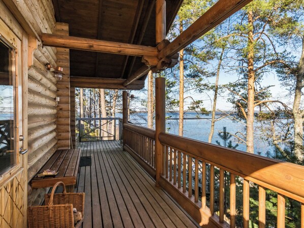 A wooden cabin with a deck overlooking a body of water, surrounded by trees.