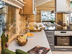 A modern kitchen with wooden cabinetry, a built-in oven, and a dining area with a table set for four. - Roopenranta by Interhome (Asikkala)