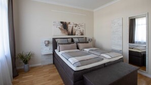Een moderne slaapkamer met een groot bed, nachtkastjes, een potplant en kunst aan de wand.