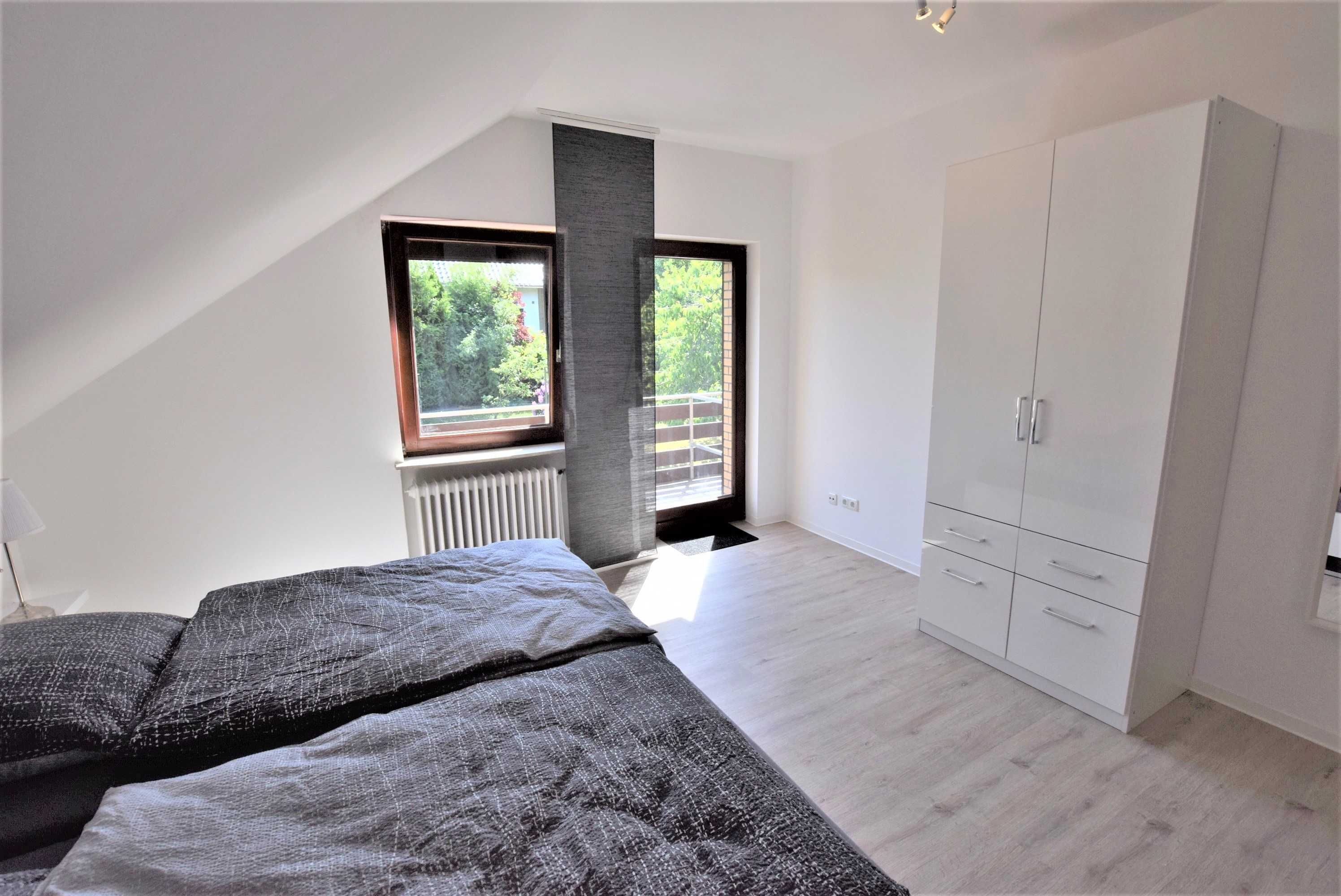 Et soveværelse med skråvæg, stort vindue, garderobeskab og radiator.