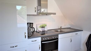 A modern kitchen with white cabinets, stainless steel appliances, a built-in oven, and a coffee maker. - Vacation apartment T & T 1 (Malente)