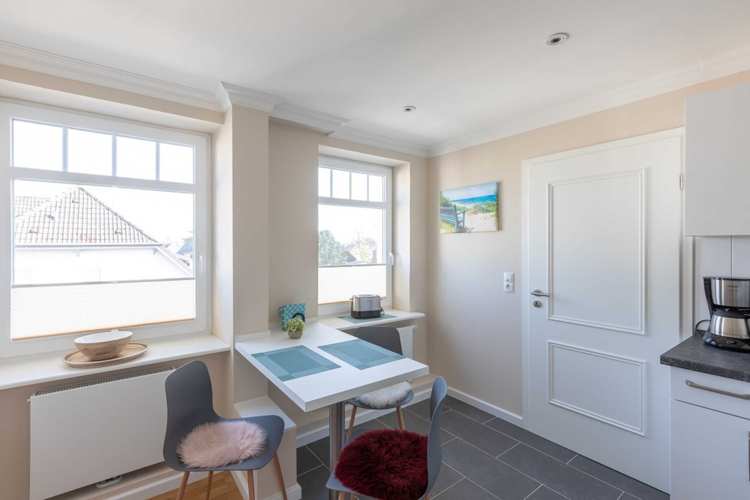 A compact kitchen with a dining area, a white door, and a view of the outside through large windows.