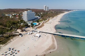 Vista aérea de um hotel à beira-mar, com piscina, guarda-sóis e um píer.