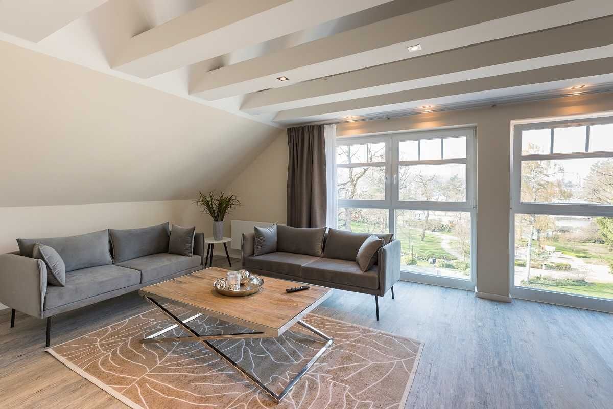 A modern living room with a grey sectional sofa, a wooden coffee table, and a large window offering a view of a garden.