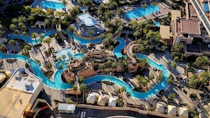 Vue aérienne d’un complexe hôtelier doté de plusieurs piscines, de palmiers et d’une installation aquatique sinueuse.