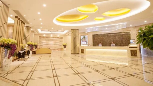 A modern hotel lobby with a reception desk, seating area, and decorative plants. - Bolailitai Hotel (Foshan)
