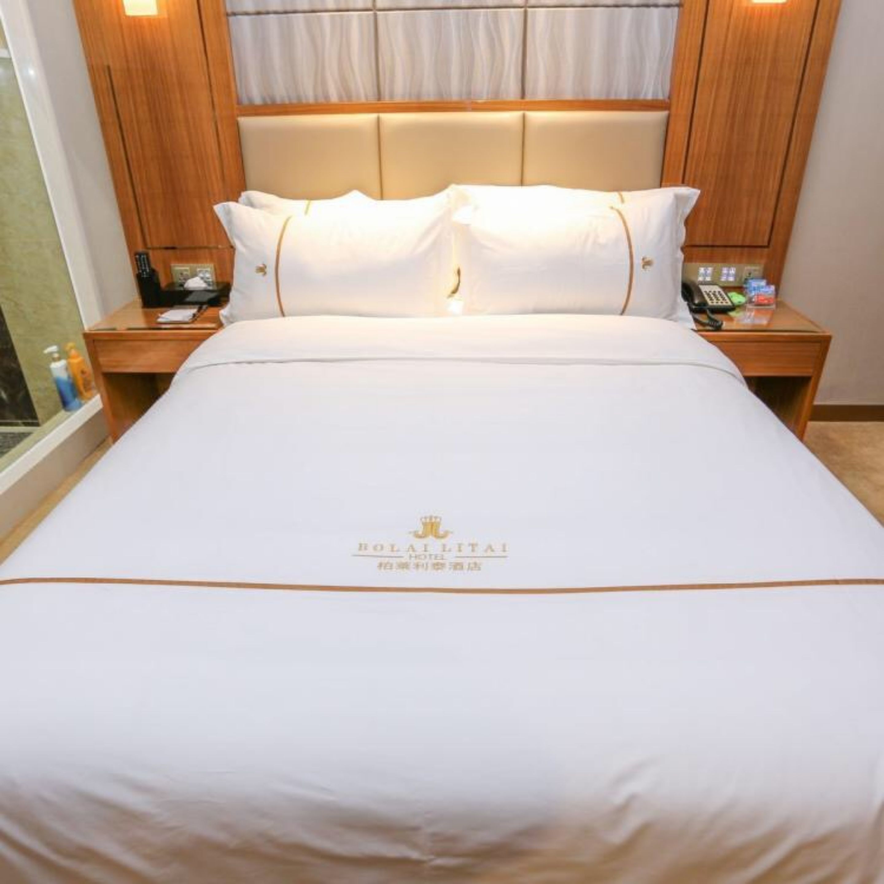 A hotel room with a large bed, wooden headboard, and a nightstand with a phone and toiletries.