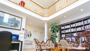 Un salón espacioso con techo alto, una escalera de madera, una amplia estantería y un escritorio con ordenador.