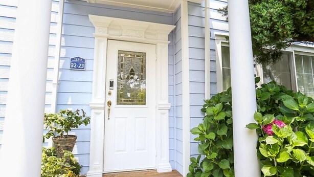 Un porche con una puerta blanca, un letrero de número de casa azul y plantas en macetas.