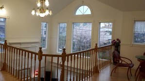 Una habitación amplia con una escalera de madera, ventanas grandes y un candelabro.