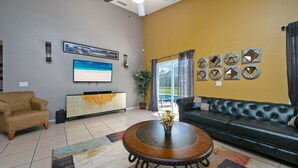 Ein Wohnzimmer mit Sofa, Sesseln, Fernseher, dekorativen Spiegeln und einer Topfpflanze.