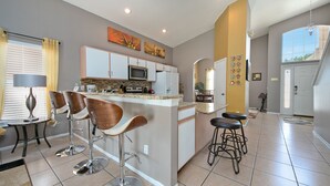 Eine moderne Küche mit Kochinsel, Barhocker und Essbereich mit Tisch und Stühlen.