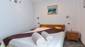 Una cama bien hecha con sábanas blancas y una manta marrón, una mesita de noche con una lámpara y un cuadro en la pared.