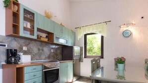 Cocina compacta con armarios azul verdoso, horno integrado, cafetera y una ventana con cortina.