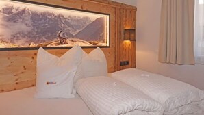 Une chambre à coucher avec une tête de lit en bois, un grand tableau encadré représentant un paysage de montagne, deux oreillers et un lit soigneusement fait.