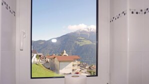 Une salle de bain équipée d’un porte-rouleau de papier toilette et d’une fenêtre donnant sur une montagne et un village.