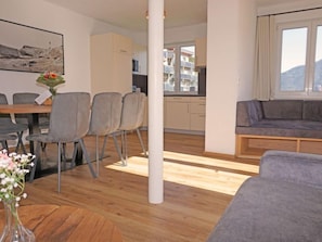 Un salon moderne avec un canapé gris, une table à manger avec des chaises, et un coin cuisine à l’arrière-plan.