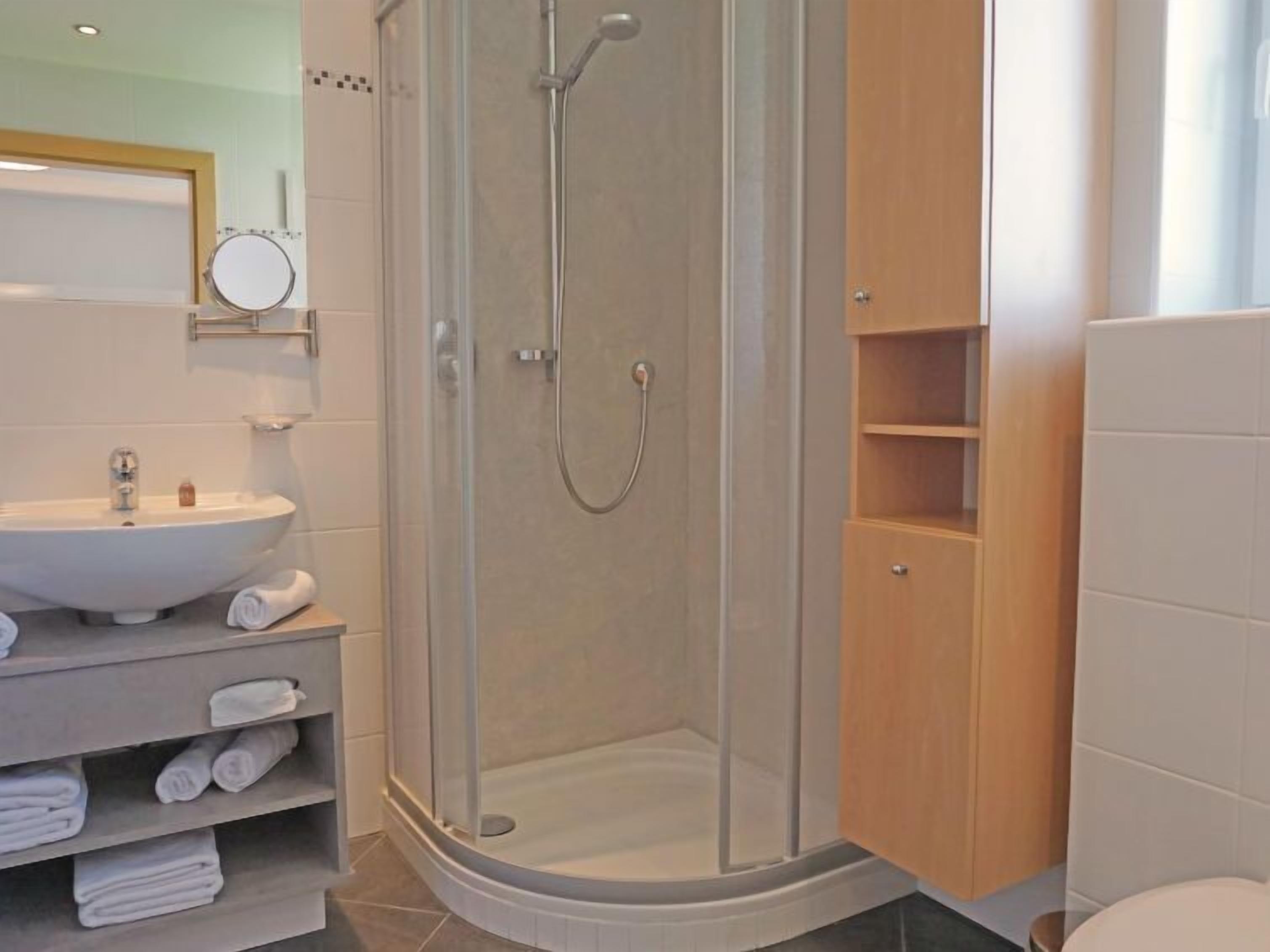 Ein modernes Badezimmer mit einer gläsernen Dusche, einem weißen Waschbecken und einem Holzkonsolentisch mit Regalen.