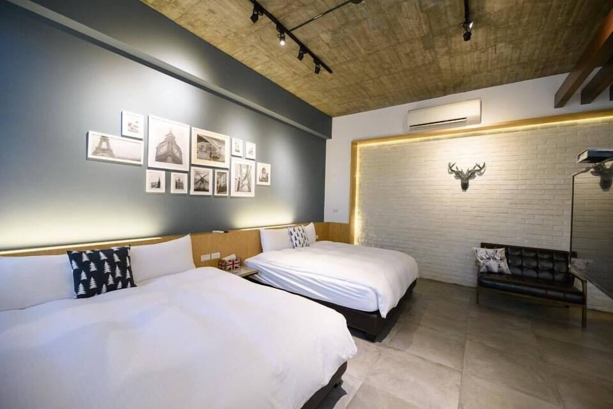 A hotel room with two beds, a brick wall with a mounted deer head, and a series of framed pictures on the wall.