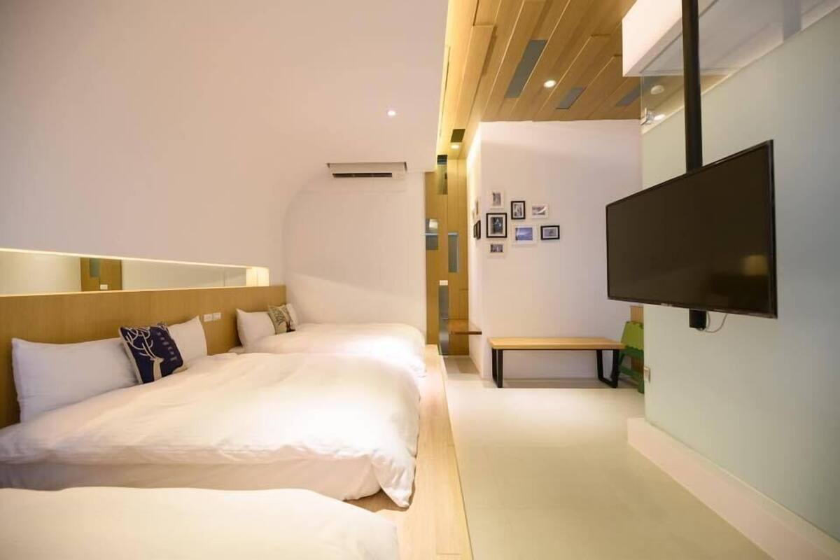 A modern hotel room with two beds, a flat-screen TV mounted on the wall, and a bench.