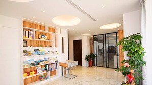 A modern hotel lobby with a marble floor, a wooden bookshelf with various books and decorative items, a small desk with a chair, and potted plants. - Peng Hu 616 B&B (Magong)