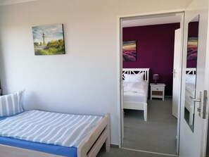 A bedroom with a bed, a nightstand, and a door leading to another room.