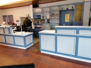 Un espace bar décoré de bleu et de blanc, avec des étagères remplies de bouteilles et de verres, et un comptoir où est affiché le menu.